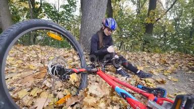 一个年轻的女人从自行车上摔下来后<strong>坐在公园里</strong>，平静膝盖的疼痛，在<strong>公园里</strong>骑一辆危险的自行车